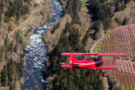 red bi-plane flying over spring river and fields near hood river, oregon